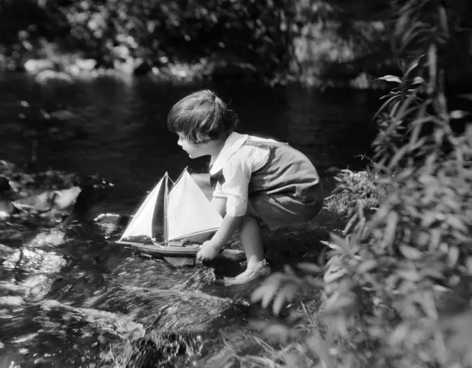 1920S Boy Putting Toy Sailboat Into Stream