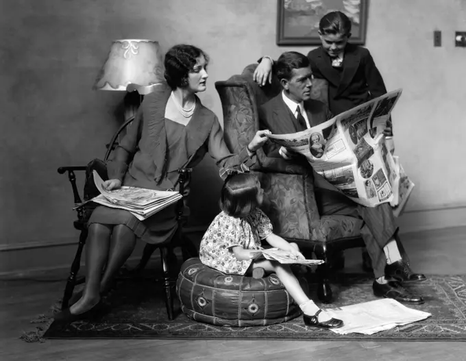 1920S Family Of Four Mother Father Son Daughter In Living Room Reading Newspaper Together Indoor