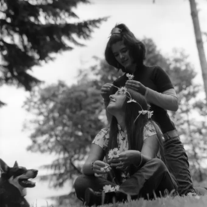 1970S Two Teen Hippie Girls Outdoors Sitting In Grass One Is Putting Flowers In Others Hair