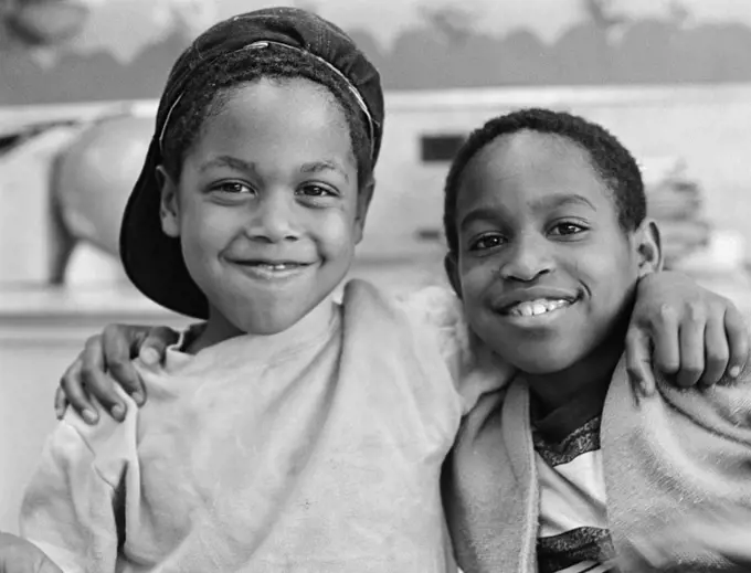 1980S Two African American Boys Smiling While Embracing Shoulder To Shoulder One Boy Has Cap On Backwards Outside
