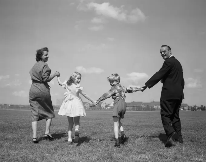 1950S Smiling Happy Family Mother Father Boy Girl Holding Hands Walking On Grass Turned Looking Back At Camera