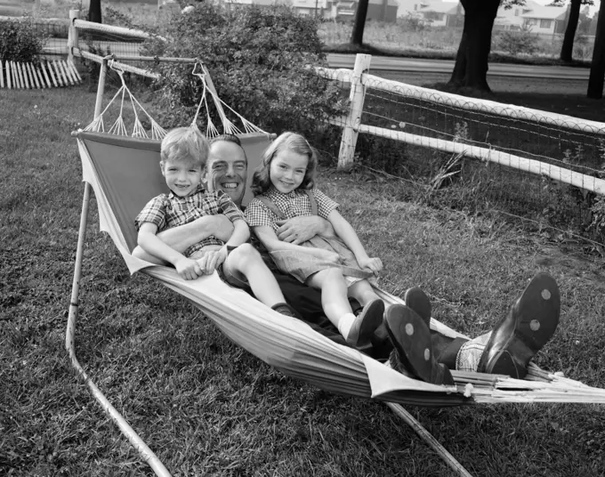 1950S Father Lying In Hammock Holding 2 Smiling Children Boy Girl