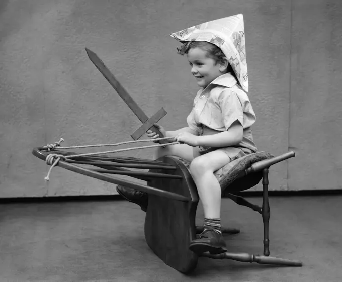 1930S Boy Playing Wooden Sword Paper Hat Riding Chair Like A Horse