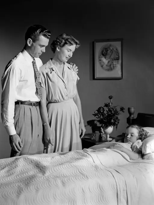 1950S Mother And Father Watching Sleeping Daughter