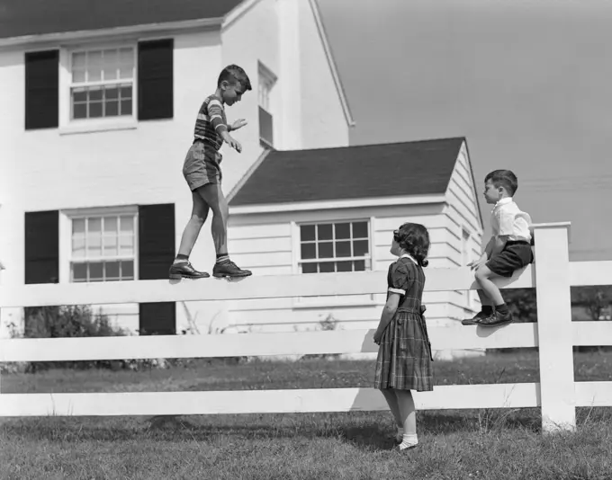 1950S Boy Walking Balancing On Fence Other Children Standing Sitting Next To Fence  