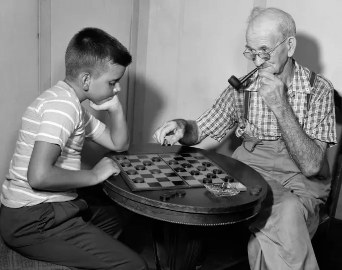 1950S Boy Playing Checkers With Grandfather Smoking Pipe & Picking Up Piece To Jump Him