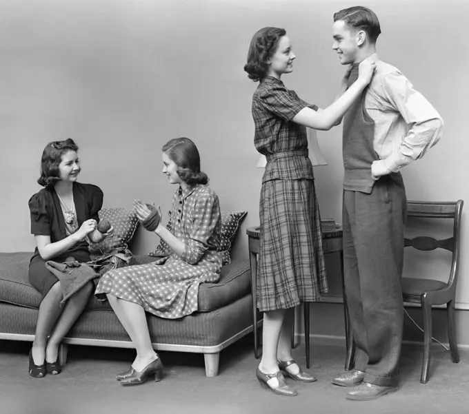 1940S Teen Group Two Girls Unwind Skein Yarn Another Girl Holds Knitted Vest Up To Fit On Boy