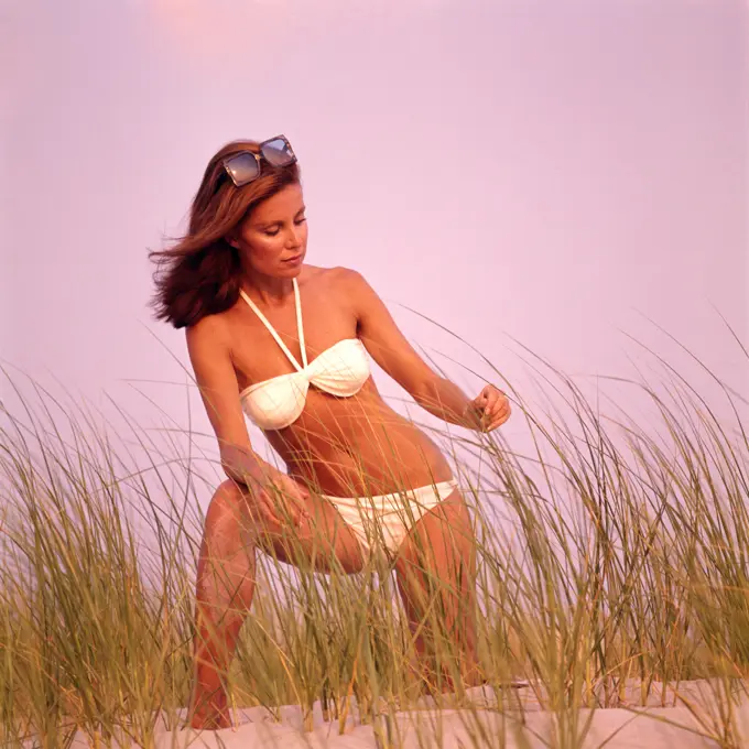 1970S Sexy Young Woman In White Bikini And Sunglasses Standing On Grassy Sand Dune