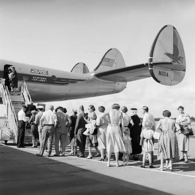 1950S Tail Of Commercial Aviation Airplane On Tarmac With Passengers In Line Waiting To Board