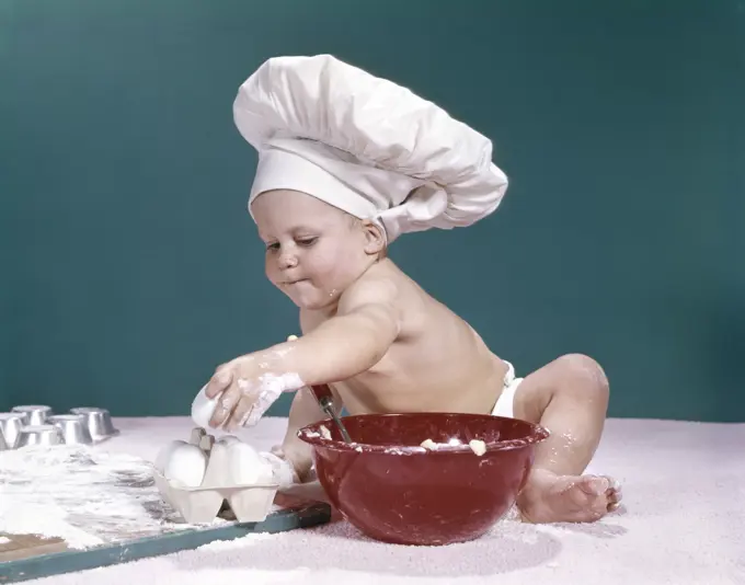 1960S Baby Wearing Chefs Hat Holding Egg Surrounded By Cooking Equipment