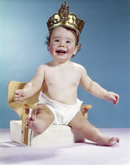 1960S Smiling Happy Baby Wearing Crown Sitting On Booster Seat Chair