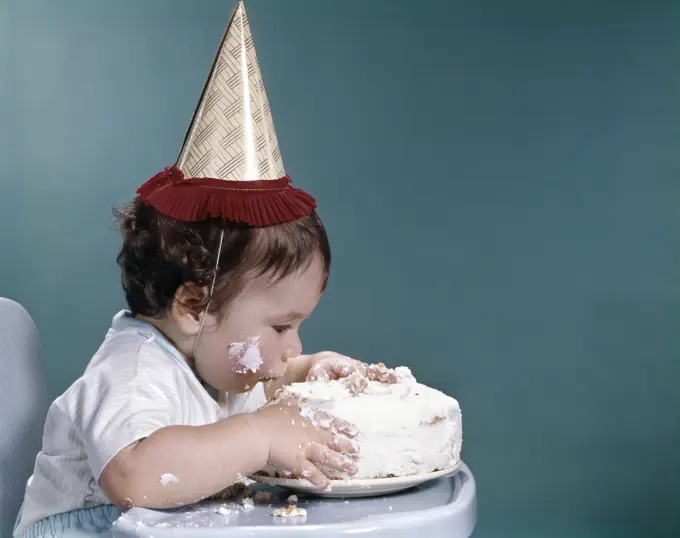 1960S Baby In Highchair Wearing Birthday Hat Eating Whole Birthday Cake