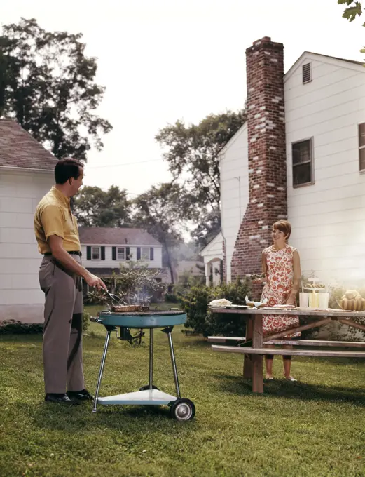 1960S Couple Suburban Backyard Man Grilling Woman Setting Picnic Table