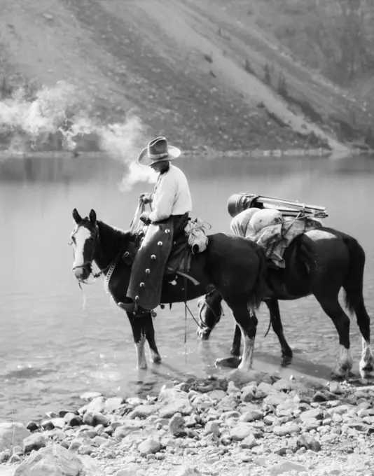 1920s 1930s MAN COWBOY ON HORSE WITH PACK HORSE BY MORAINE LAKE ALBERTA CANADA