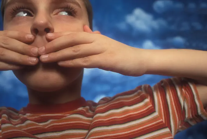 BOY WEARING STRIPED SHIRT COVERING MOUTH WITH HANDS PAINTED CLOUDS BACKDROP