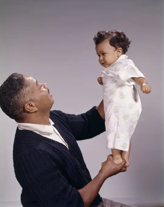 1970s AFRICAN AMERICAN FATHER HOLDING HIS BABY DAUGHTER UP IN THE AIR