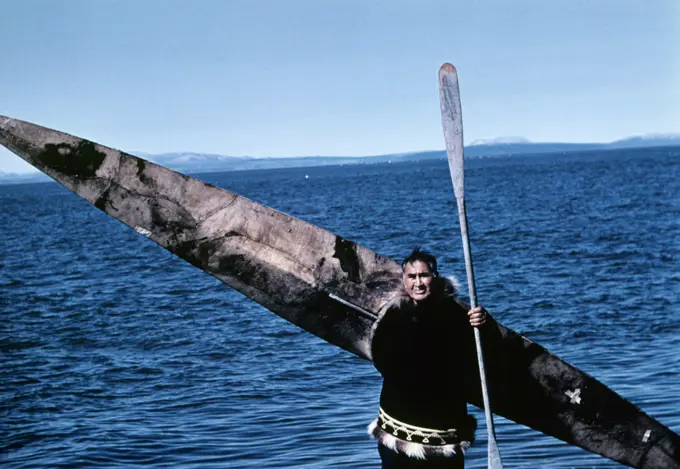 1960s INUIT NATIVE AMERICAN INDIAN MAN HOLDING SKIN KAYAK AND PADDLE WEARING PARKA LOOKING AT CAMERA KOTZEBUE ALASKA USA