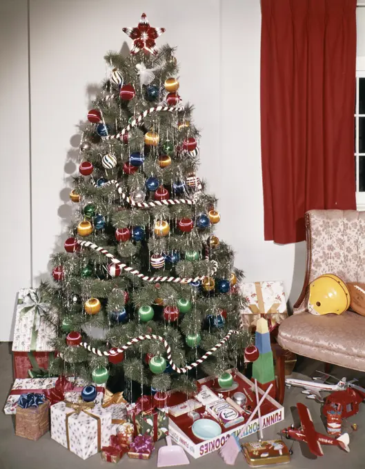 1960s PRESENTS AND TOYS UNDER CHRISTMAS TREE DECORATED WITH ORNAMENTS GARLANDS AND TINSEL