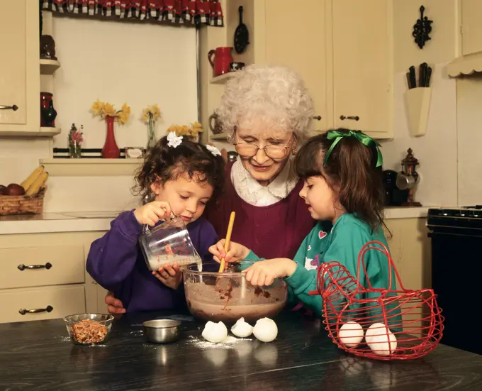 GRANDMOTHER WITH GRANDDAUGHTERS COOKING IN KITCHEN