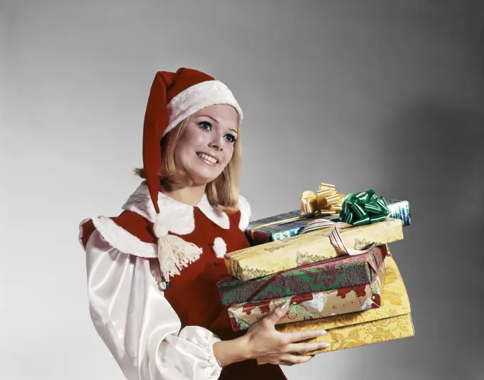 1960S Young Woman In Red And White Santa Helper Costume And Hat Holding Pile Of Wrapped Christmas Presents Studio