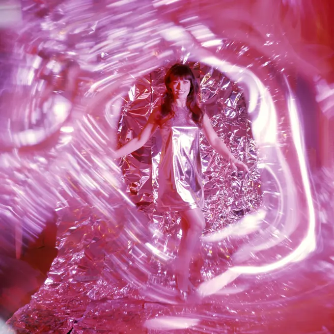 1960S 1970S Smiling Woman With Long Brunette Hair In Short Silver Lame Miniskirt Dress Dancing Amid Swirling Red Light And Foil Backdrop