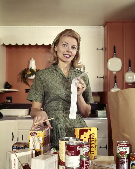 1960S Young Blond Housewife Smiling While Checking Grocery Shopping Receipt In Kitchen