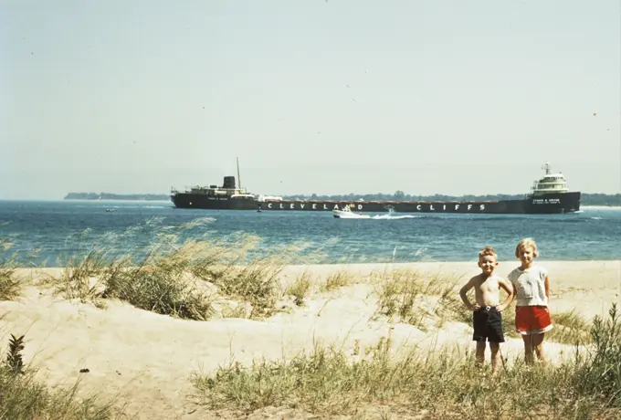 1950S Young Boy And Girl On Beach Smiling With A Tanker Ship On Lake Behind Them Port Huron Michigan 1955