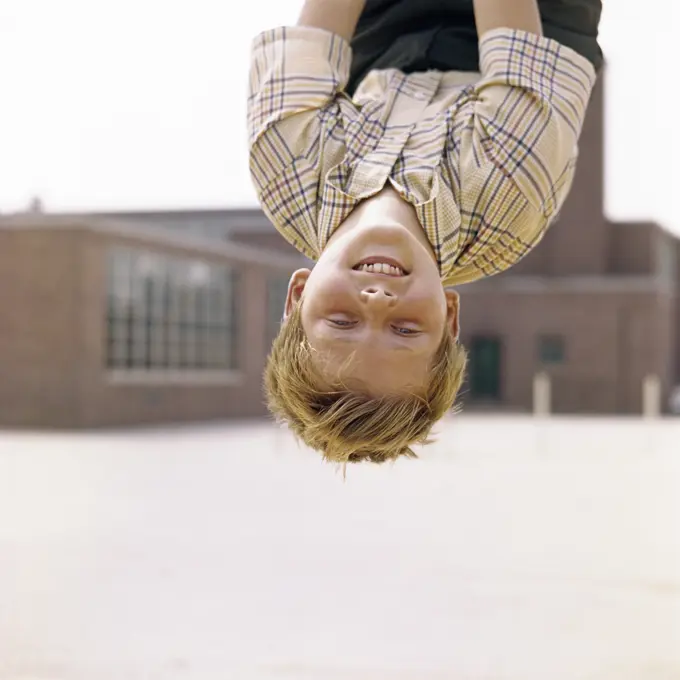 1960S Smiling Red Haired Boy Hanging Upside Down In Elementary School Yard