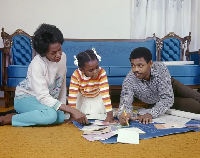 1960S 1970S African American Family Sitting On Living Room Floor Looking At New House Blueprints And Paint Chips