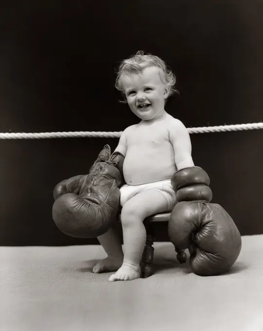 1930S Smiling Baby Seated On Stool In Boxing Ring Wearing Oversized Boxing Gloves Wearing Diaper