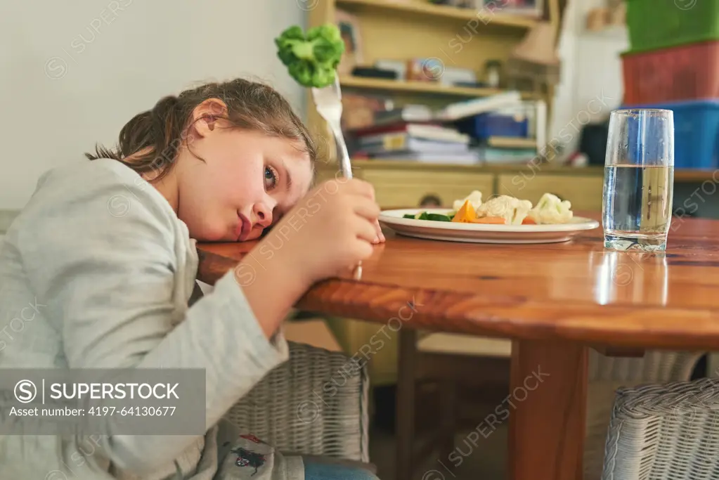 Angry, child and eating healthy food in home with vegetables, nutrition and tired of green diet. Hungry, kid and frustrated with plate of broccoli, salad and dislike for vegan dinner or choice