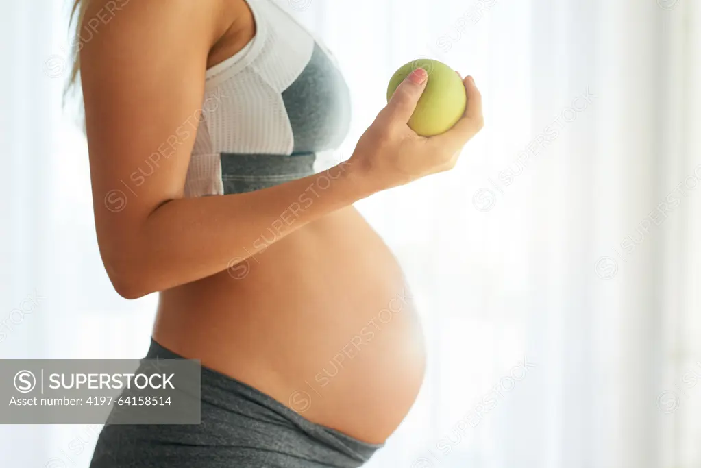 Pregnant, woman and apple for stomach in home, maternity and healthy diet for fetal nutrition. Pregnancy development, prenatal snack and fiber for gestation, obstetrician recommendation for wellness