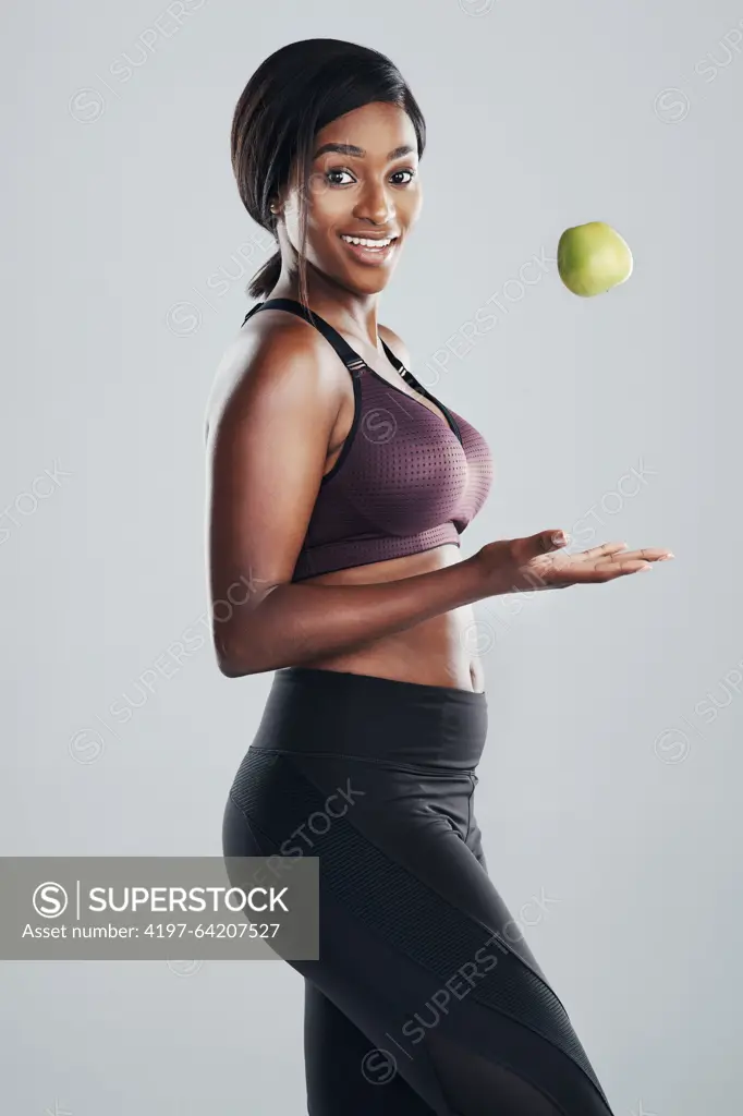 Black woman, portrait and fitness with apple in studio for healthy body, nutrition and weight loss. Slimming, happy and person throwing fruit by gray background for vitamin c, detox and vegan diet