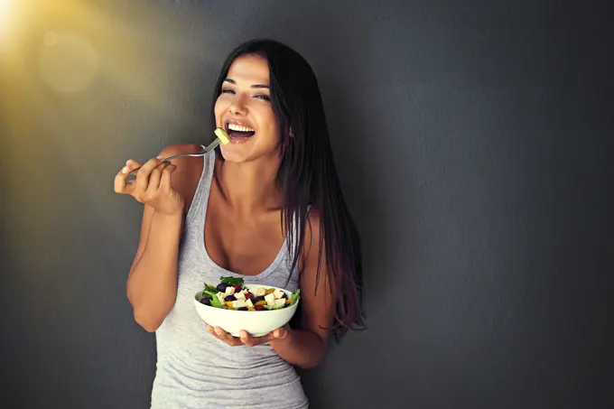 Happy woman is eating a salad, healthy food and nutrition, portrait and vegetables isolated on wall background. Organic, vegan and health with diet, female model to lose weight with mockup space