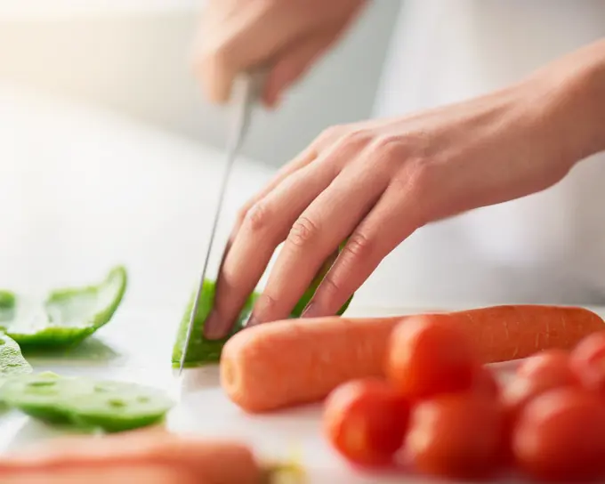 Cooking, hands and knife for vegetables on counter in kitchen of home for diet, health or nutrition. Chef, food and recipe ingredients with person preparing organic meal for dinner or wellness