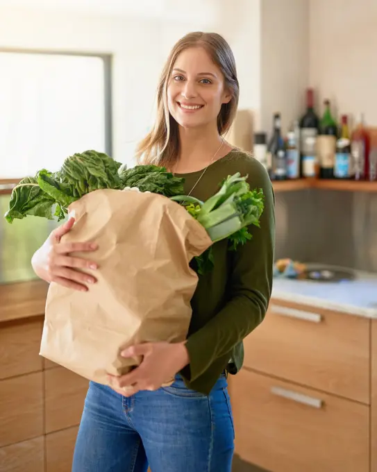 Happy, woman and portrait with vegetables in kitchen for grocery shopping, healthy cooking and eating. Female person, smile and bag of ingredients with spinach or lettuce for nutrition and vegan diet