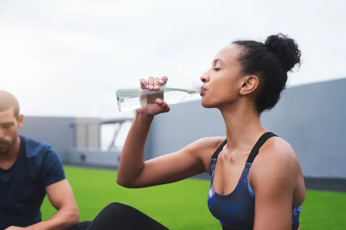 Couple, drinking water and woman with fitness, relax and nutrition with wellness, healthy and aqua. People, outdoor and athlete with liquid, bottle and balance diet with workout, training or exercise