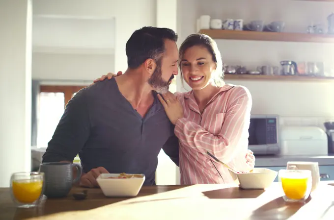 Happy couple, hug or eating breakfast with cereal, diet or juice in morning meal in house kitchen. People, trust or snack in bowl for bonding, funny joke and food in healthy marriage or love together