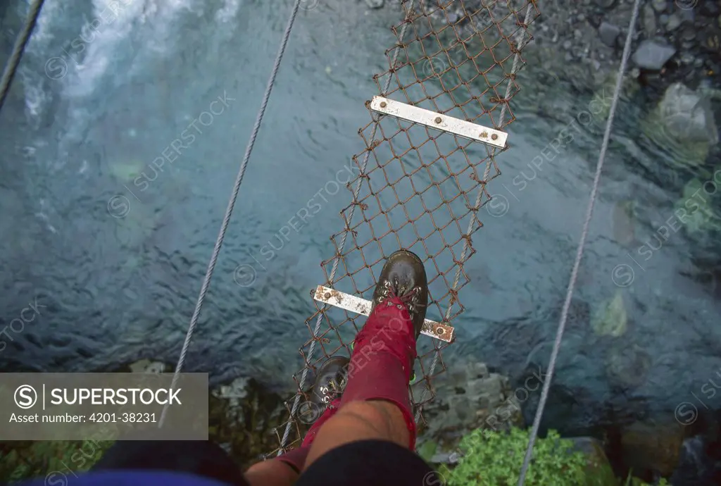 Hiker crossing wire bridge, Tuke River, New Zealand