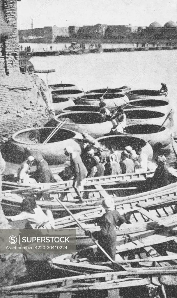 Gufa and Bellum boats awaiting hire on the River Tigris, which splits Baghdad, Iraq, in half. A gufa is a circular boat propelled by a pole or single paddle, rather like a coracle. This model represents a Baghdad gufa from 1930. The round basketry hull is constructed from ribs of wood from the pomegranate tree, interwoven with rope made from date-palm leaves and a rail of tamarisk roots. The outer surface of the gufa is made watertight by a coating of bitumen.     Date: circa 1920