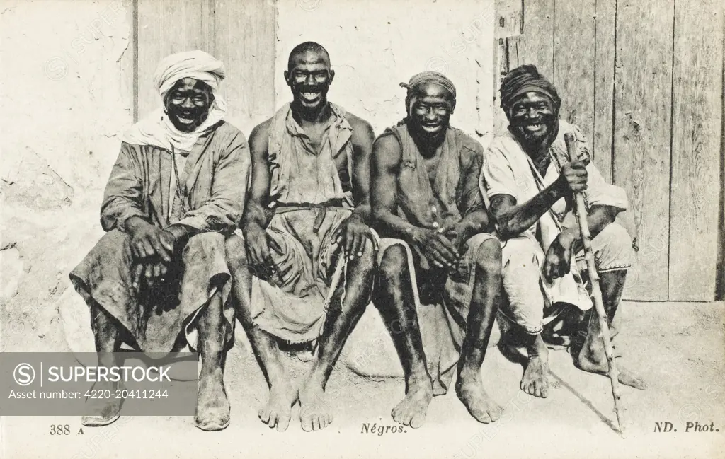 Four happy black Algerians, seated outside a building.     Date: 1910s