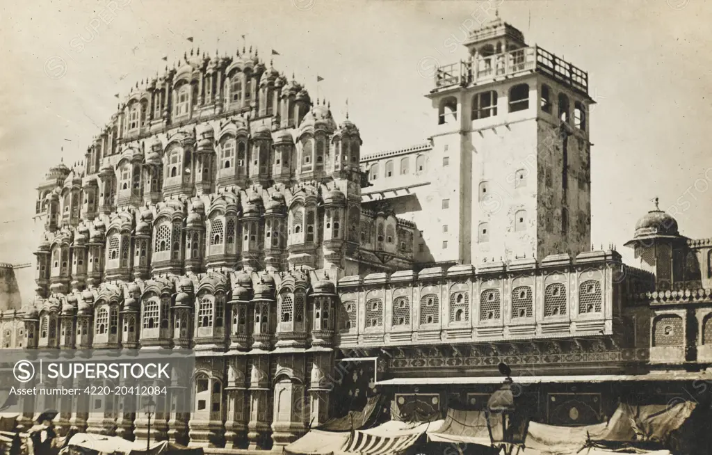 Hawa Mahal, a palace in Jaipur, India. It was built in 1799 by Maharaja Sawai Pratap Singh, and designed by Lal Chand Usta in the form of the crown of Krishna, the Hindu god. It forms part of the City Palace and extends the Zenana or women's chambers, the chambers of the harem. Its original intention was to allow royal ladies to observe everyday life in the street below without being seen. It has five stories and is constructed of red and pink sandstone, highlighted with white quakeee quick lim