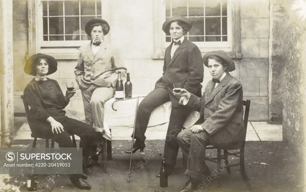 Group of Transvestite Ladies. Four women dressed as men lounge around a table, drinking champagne and beer and dressed in sharp men's suits nd soft hats. The lady of the left appears to be wearing a fisherman's jumber and is smoking a curved pipe.     Date: circa 1910s