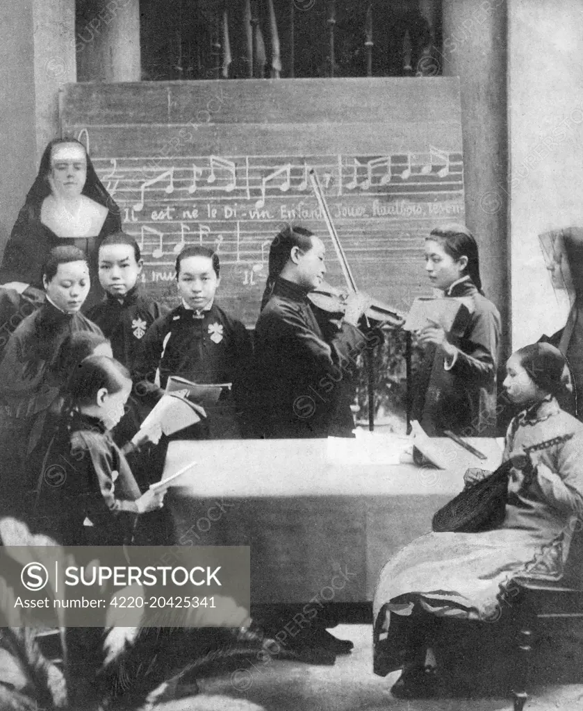 Young Chinese girls at a Roman Catholic school of music in Canton, being  taught to play Christmas carols by French nuns. Date: 1911 - SuperStock