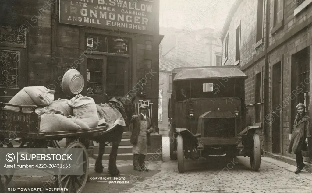 Old Towngate, Holmfirth, West Yorkshire. Holmfirth has become well known as the location of the situation comedy Last of the Summer Wine. A wagon of corn merchants and millers Gledhill &amp; Brook can be seen on the left, waiting for a large truck to pass through a (rather narrow) street.     Date: circa 1910s