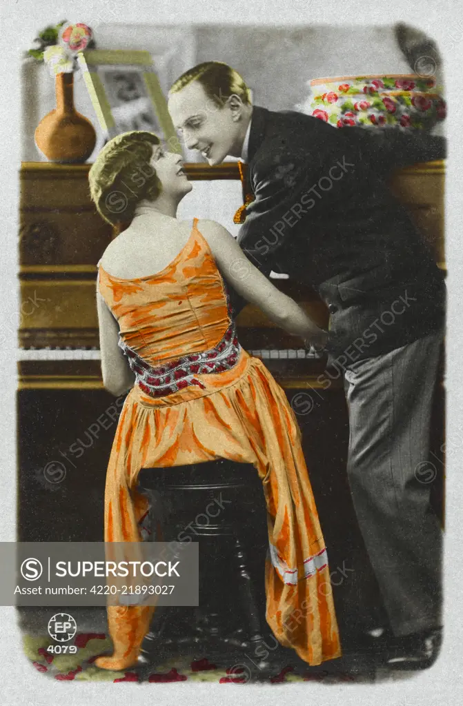  A lady plays the piano to  entertain her gentleman  friend: practice makes  perfect.      Date: 1920s