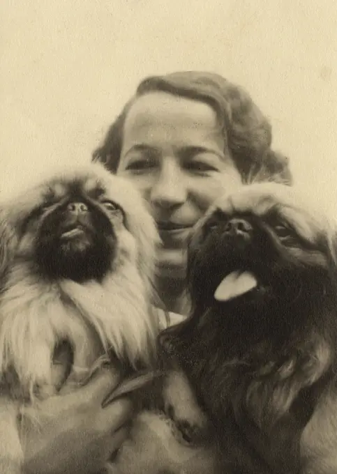 Woman with two Pekingese dogs in a close-up photo.      Date: circa 1930s