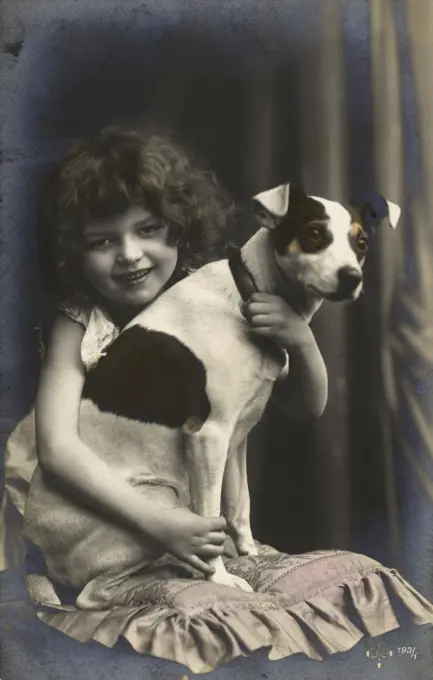 Studio portrait, little girl hugging her terrier dog, France.      Date: circa 1910s