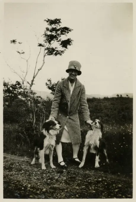 Woman in a garden with two collie dogs.      Date: circa 1930s