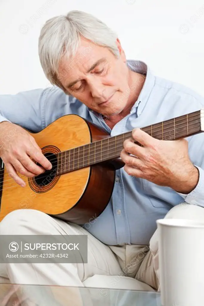 Elderly man on couch playing acoustic guitar